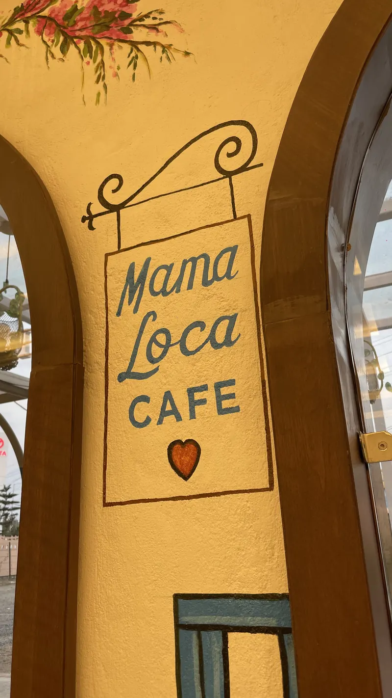 A painted hanging cafe sign under a wooden arch