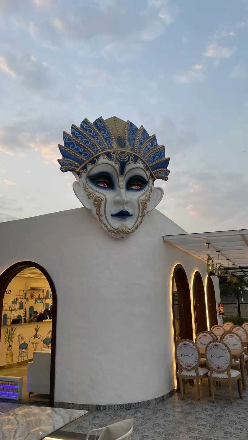 The mask over the lit arcade at dusk, with tables set under the arches