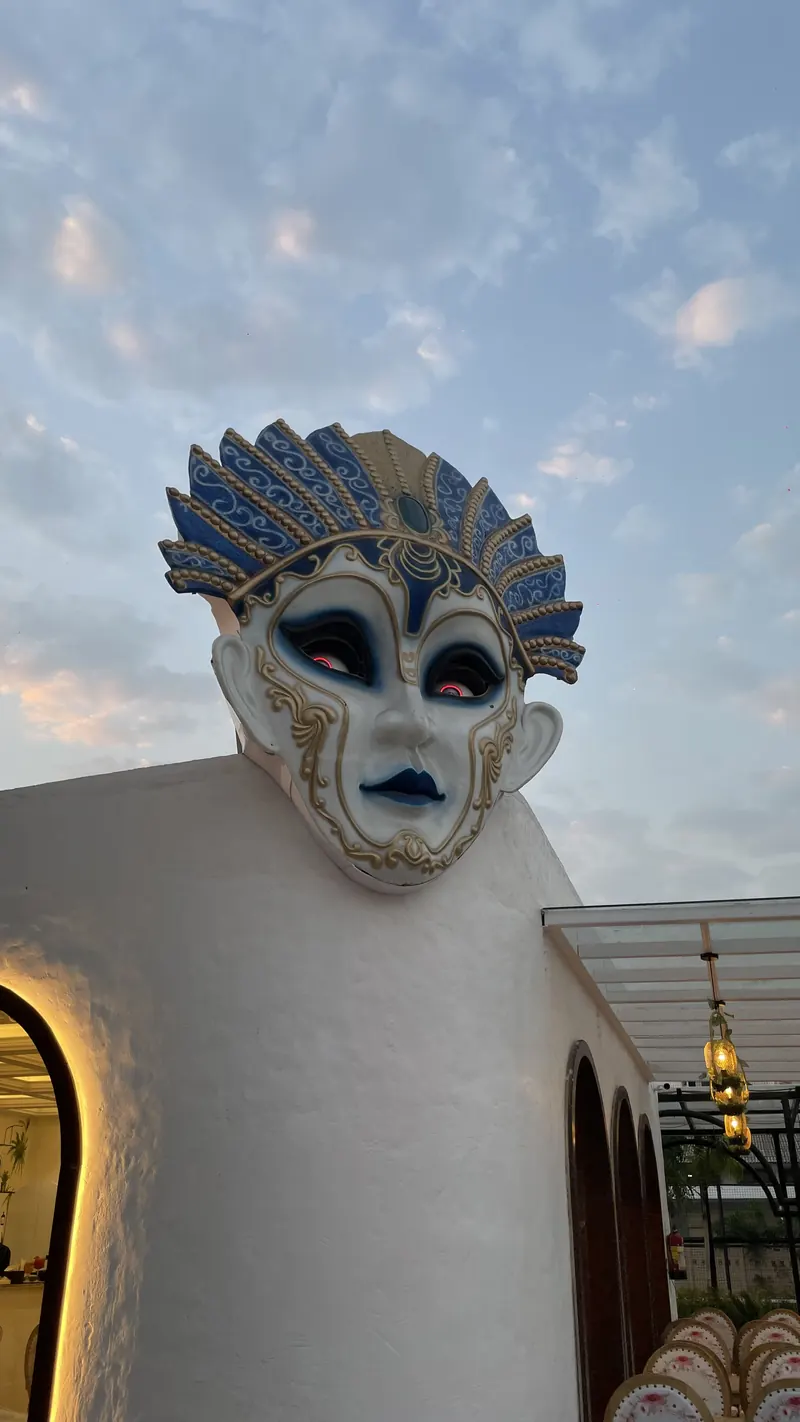 The painted Venetian mask above the whitewashed entrance, against an evening sky