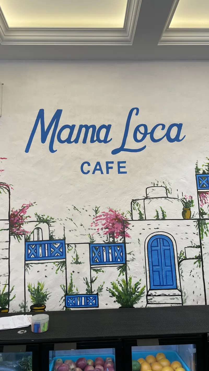 The hand-painted mural wall: Mama Loca Cafe above a whitewashed village with blue doors